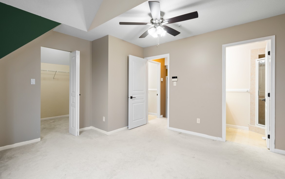 Large primary bedroom with ceiling fan, walk in closet, ensuite bathroom and vaulted ceilings.