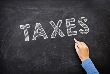 The word Taxes written on a chalk board in block letters with a hand holding a piece of talk underneath the word.